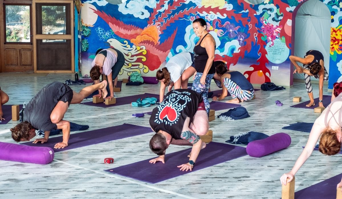 Group yoga class in a colorful indoor setting with a mural on the wall.