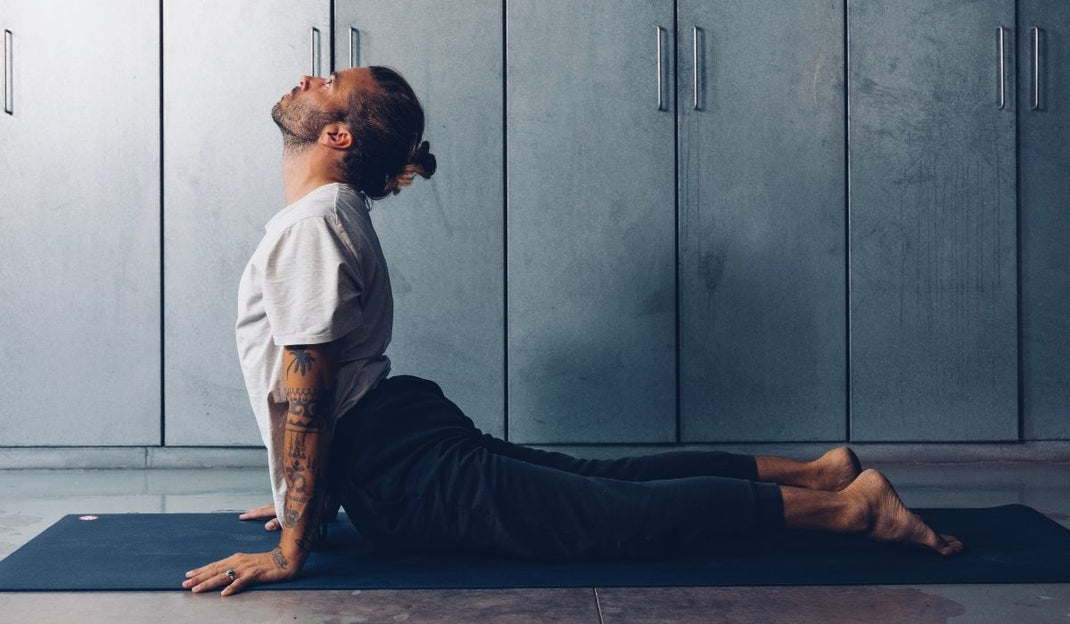A person performs the Cobra pose on a yoga mat in a minimalist indoor space with gray walls and cabinets.
