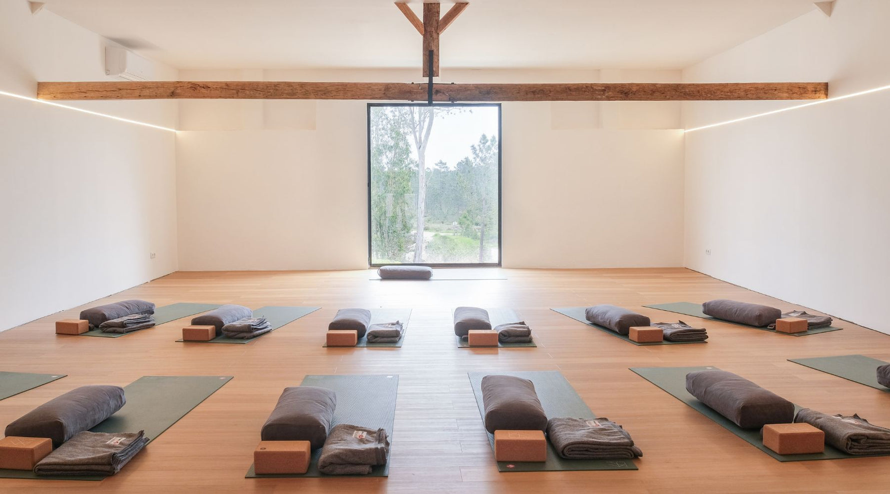 Casas Na Ferraria's light inside studio space with 12 PROlite yoga mats facing a large window in the front center of the room. each yoga mat has a bolster, cork block and blanket available for the yoga practice