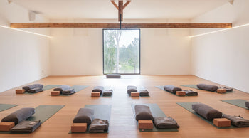 Casas Na Ferraria's light inside studio space with 12 PROlite yoga mats facing a large window in the front center of the room. each yoga mat has a bolster, cork block and blanket available for the yoga practice