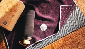 Purple hot yoga towel with a cork block and water bottle on it.
