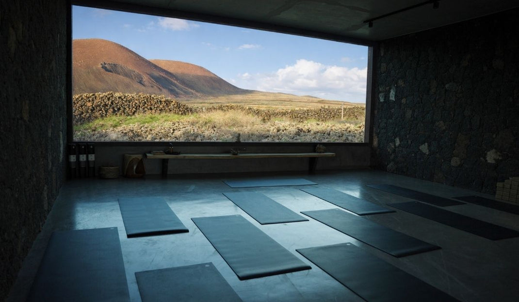 Yoga studio with mats laid out on the floor, featuring a large window view of rocky hills and blue sky outside.