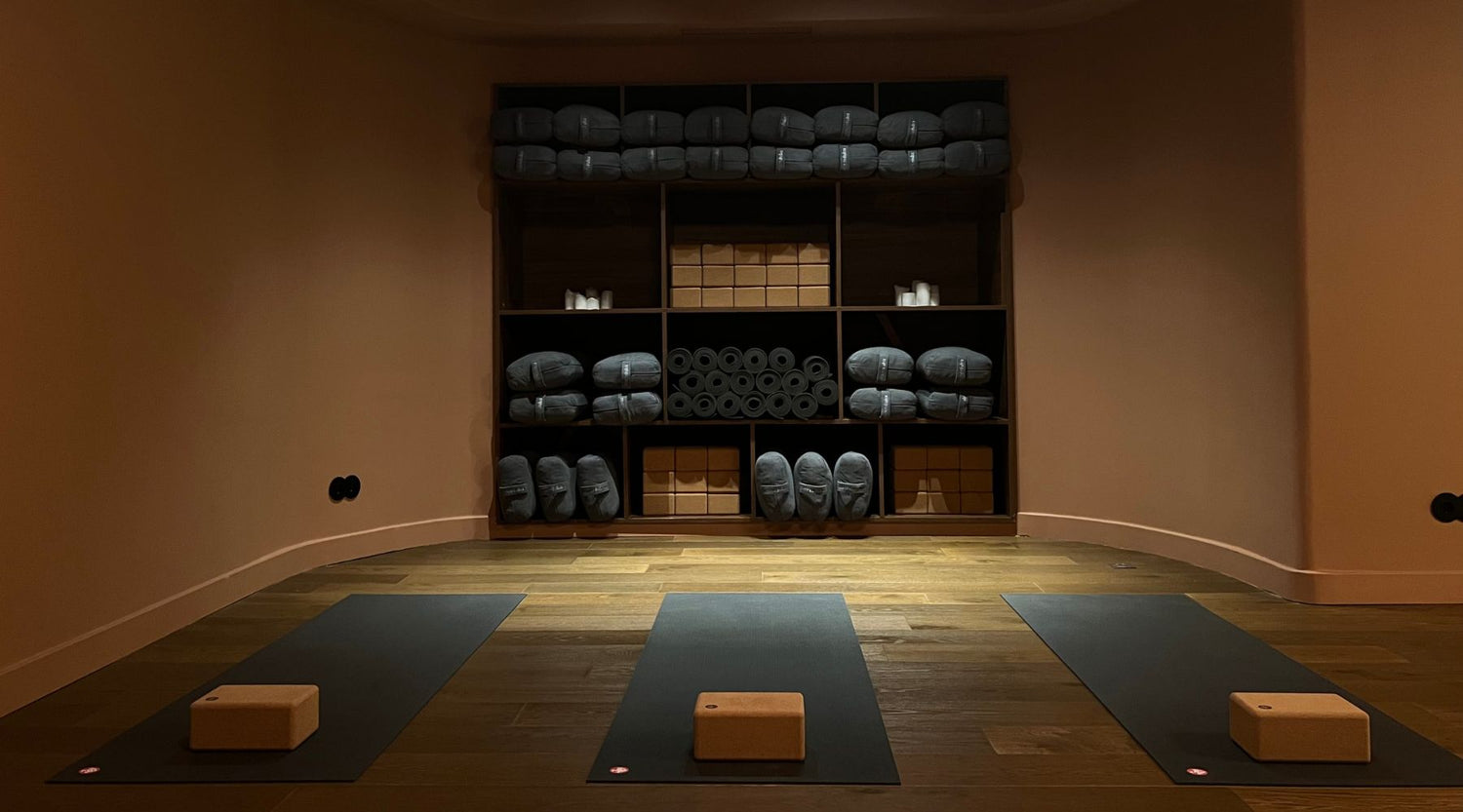 Serene Leela Lisboa yoga studio featuring three mats, a cork block on each, and neatly organized yoga props on shelves in warm light.