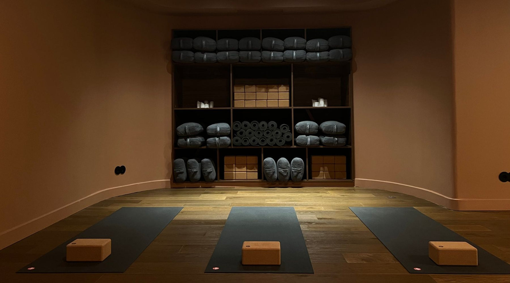 Serene Leela Lisboa yoga studio featuring three mats, a cork block on each, and neatly organized yoga props on shelves in warm light.