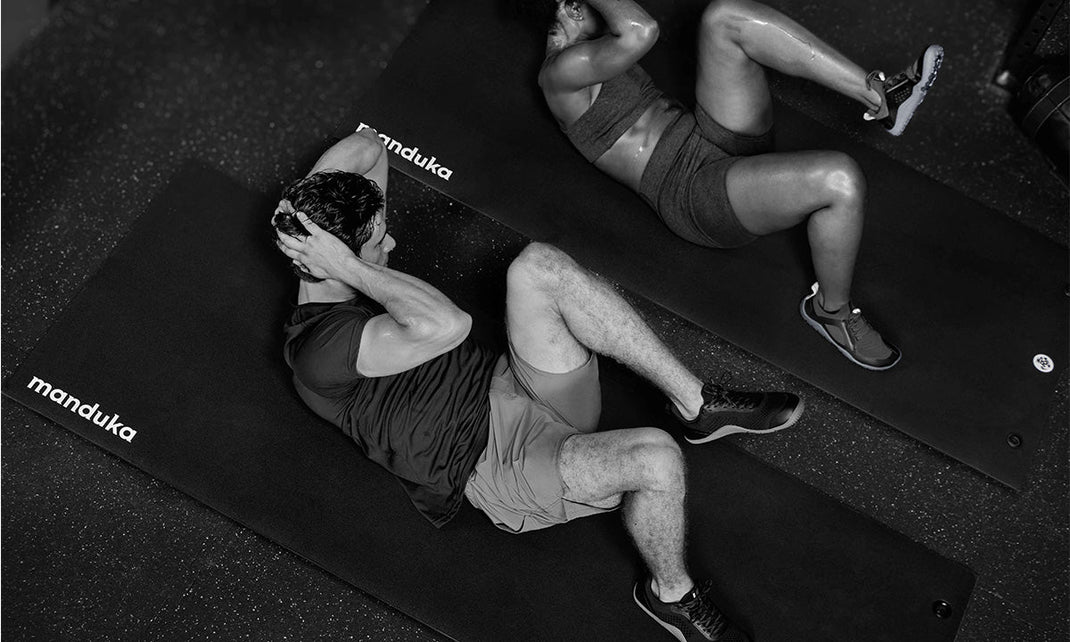 Two people doing abdominal crunches on exercise mats in a gym, viewed from above.