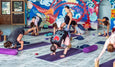 Group yoga class in a colorful indoor setting with a mural on the wall.
