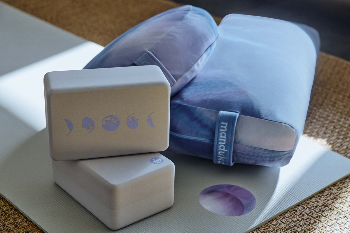 Manduka yoga setup with a blue bolster two foam blocks and a gray yoga mat in soft natural light
