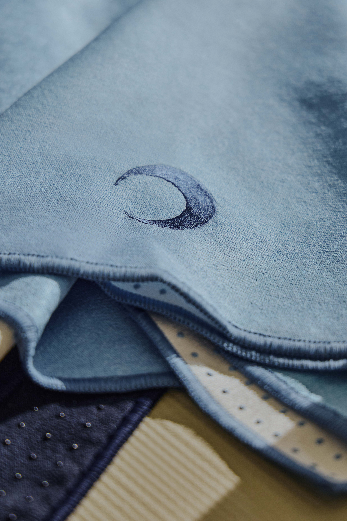 Close up of layered Manduka yoga mats in blue and black with textured surfaces stitched edges and a subtle circular logo