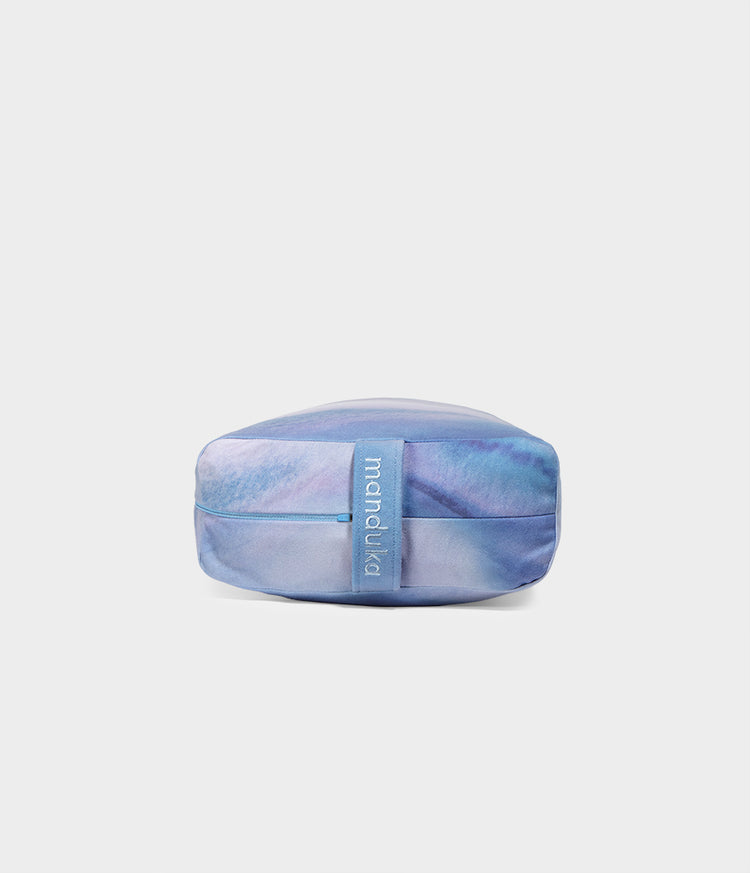 Manduka blue rectangular bolster for restorative yoga and meditation with a structured supportive shape and central carry strap on a light background