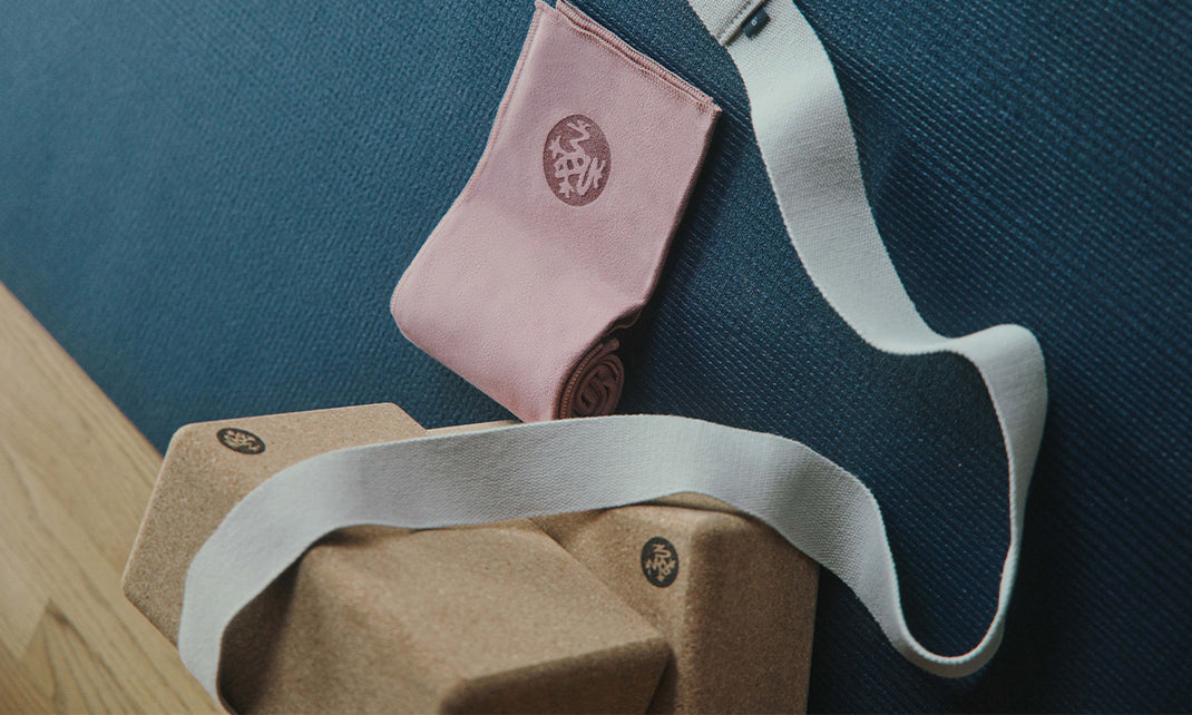 Manduka yoga straps and cork blocks in beige, pink, and white arranged on a dark textured surface