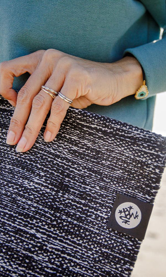 Close up of a hand resting on a folded black and white Manduka yoga mat with a logo patch