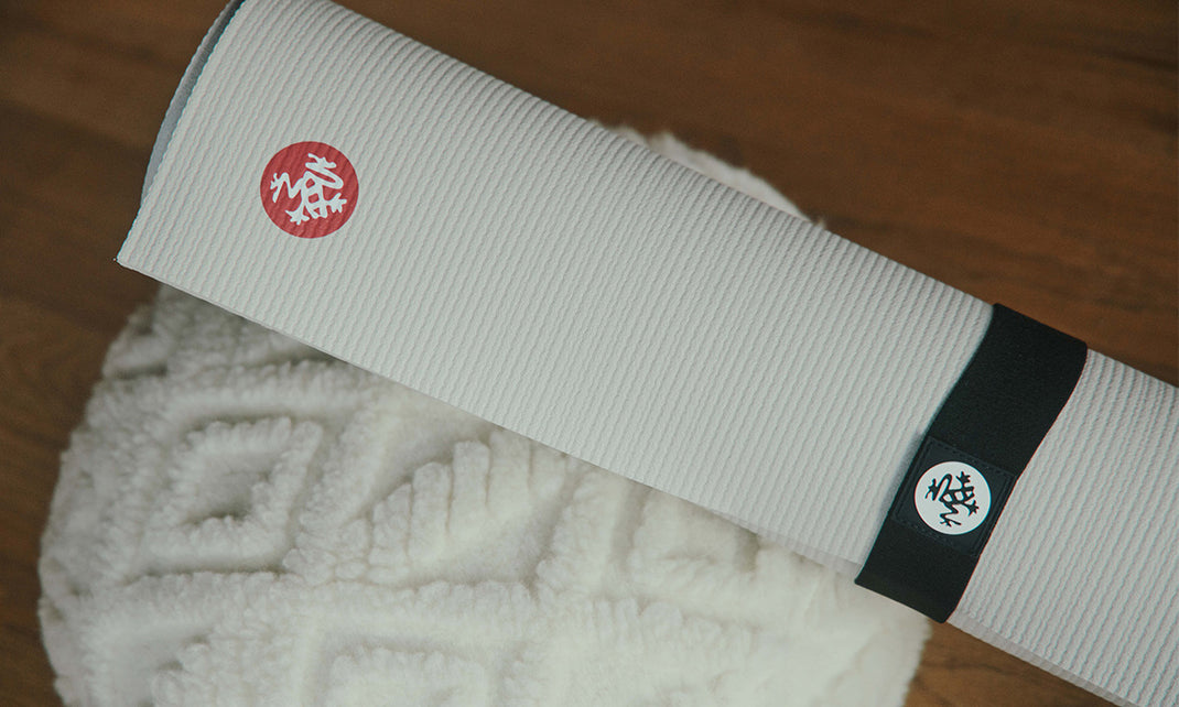 Manduka white yoga mat rolled on a textured white blanket with a contrasting black band and circular logos