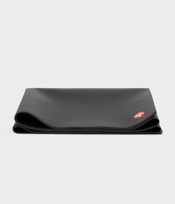 Folded black Manduka yoga mat with a textured surface and curved rolled edges on a light background